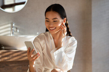 Attractive young asian woman reading beauty blog online, using smartphone
