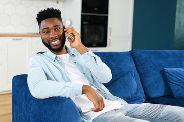 Serene handsome calm guy talking on the smartphone while sitting on the comfortable sofa at stylish apartment. Portrait of multiracial man during phone conversation