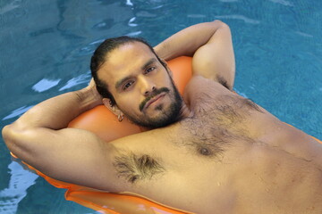 Very sensual ethnic man sunbathing in swimming pool 
