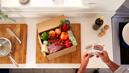 Overhead Of Man In Kitchen Holding Recipe Cards For Online Meal Food Recipe Kit Delivered To Home