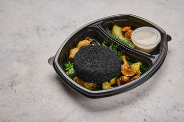 Close up rabbit cutlet in black breading in baby potatoes, spinach and mushrooms in black plastic container on light background. Designer food concept for take away or delivery