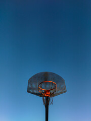 Orange basketball basket seen from the front with rusty metal net and blue sky in the background