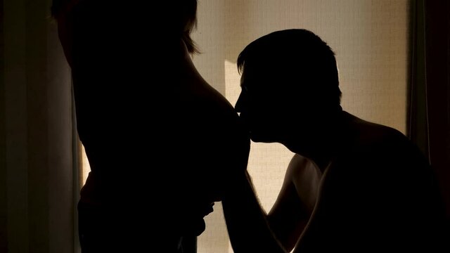 Husband Kisses Pregnant Wife Tummy Silhouette Against Window And Roll Curtains