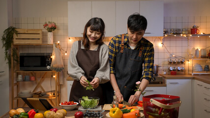 cheerful asian romantic couple shaking body left and right to the music while they are making valentine’s dinner together in the kitchen at home
