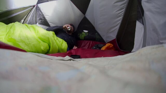 A man inside a tent drinking beer wearing a hat