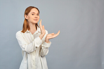 Portrait of cute young girl holding hand pointing to ads with her index finger on gray background.