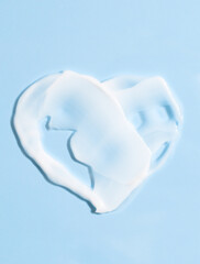 Smears of cream on a blue background in the shape of a heart. White cosmetic texture for skin care, top view. Health care, beauty concept.