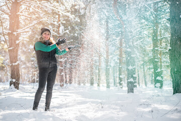 Woman surrounded by snowflakes. Model throws up snow in winter forest. Toned image.