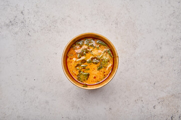 Tom Yam soup with salmon and seafood in a paper solid container on light background. Designer food concept for take away or delivery