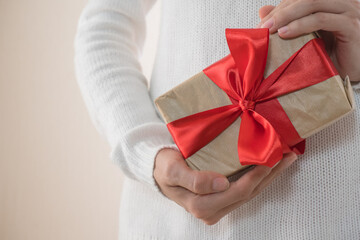 Gift with a red ribbon in female hands, giving a surprise gift box. Boxing day, holiday, birthday, christmas, mother's day.