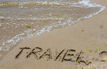 Travel concept - inscription in the sand. Sandy coast of the sea. Motivation. Ocean wave. The word travel is written on the sea beach. Vacations on the shore