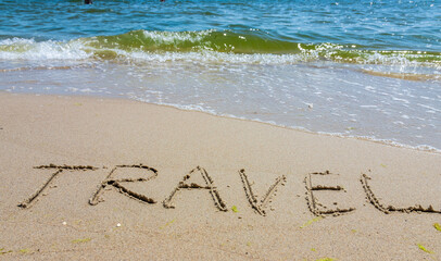 Travel concept - inscription in the sand. Sandy coast of the sea. Motivation. Ocean wave. The word travel is written on the sea beach. Vacations on the shore