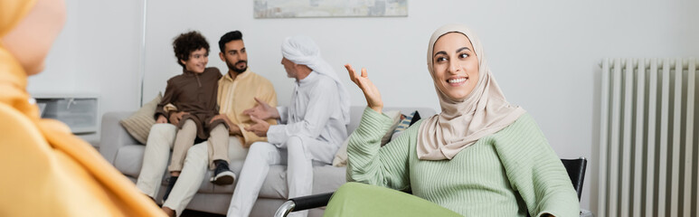 happy muslim woman talking to blurred mother near interracial family at home, banner.