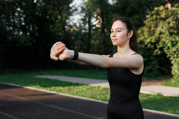 A fitness woman doing a stretching exercise stretches her triceps and shoulders. Women stretch to warm up before running or training. In the park, on the sports field.