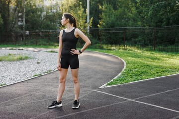 a Caucasian woman is resting after sports. A woman is sitting on the floor in a park, on a sports field. A tired young woman is resting after a run in the fresh air.