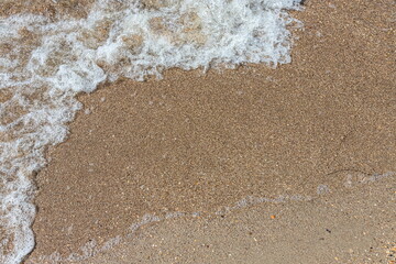 Close-up of sea foam on the sand beach with summer sunlight