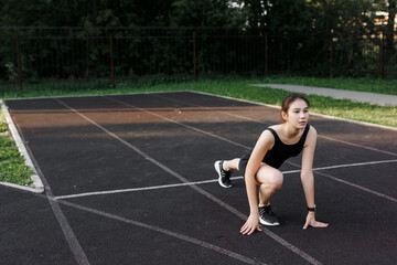 A fitness woman doing a stretching exercise stretches her legs. Women stretch to warm up before running or training. In the park, on the sports field. side view, yoga elements.