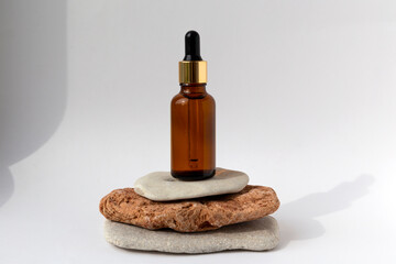 Tower from multi-colored stones with a brown oil bottle with a pipette on a white background. Natural podium with cosmetics