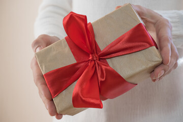 Gift with a red ribbon in female hands, giving a surprise gift box. Boxing day, holiday, birthday, christmas, mother's day.