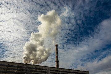 White and gray smoke and steam from a high concrete chimney against the bright blue sky