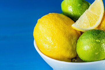 Whole and sliced lemons and limes in a white plate close-up macro on a blue background.