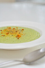 Vegetarian diet and vegan food, green healthy broccoli soup on a plate on a clean kitchen table. Tasty and nutritious meal, lunch or dinner with turmeric and chili on top.