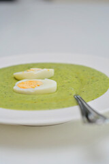 Vegetarian diet and vegan food, green healthy broccoli soup on a plate on a clean kitchen table. Tasty and nutritious meal, lunch or dinner