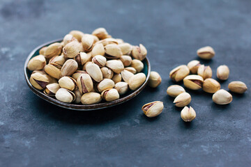 A  plate with raw pistachios in a shell shell on a dark gray background