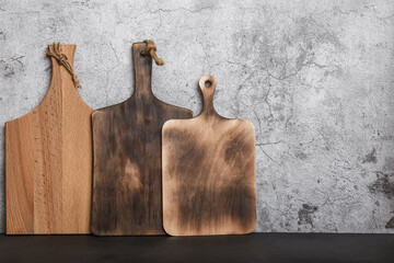 Samples of three different rustic wooden cutting boards on a kitchen countertop against a concrete...
