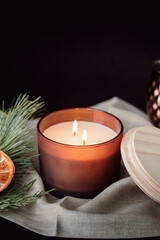 Christmas Still Life.  Close Up Lit Double Wick Candle with Dried Oranges and Berries Against Dark Background. Moody and Warm Holiday Candle. Vertical Image with Copy Space.