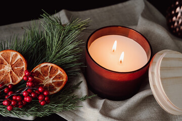 Christmas Still Life. Lit Double Wick Candle with Dried Oranges and Berries Against Dark Background. Moody and Warm Holiday Candle.