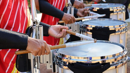 Hands with drum sticks and drum. Lines of men in red shirts practicing playing snare marching drums...