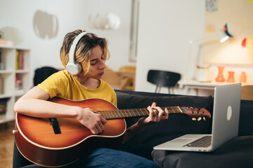 teenager boy playing acoustic guitar at home. he has online lesson