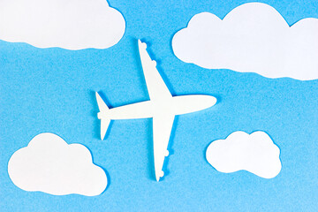 White plane model on light sky blue background with paper clouds top view flat lay.