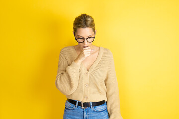 Young beautiful woman wearing casual sweater over isolated yellow background with her hand to her mouth because she's coughing