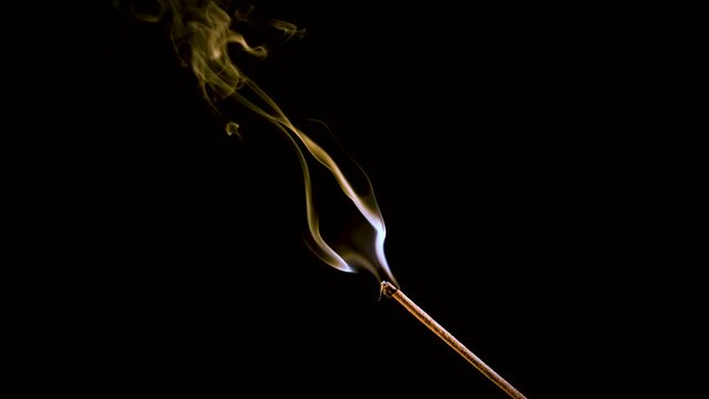 An aroma stick burns and smokes. Colored smoke is filmed in slow motion and close-up.