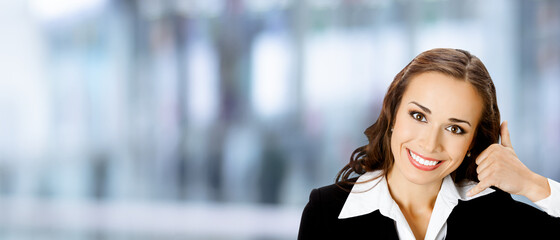 Businesswoman in black suit showing call me hand sign gesture, over blurred modern office interior...