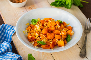 Boiled white rice with fried pumpkin cubes, onion and spices in a round gray plate on a wooden tray. Pumpkin recipes