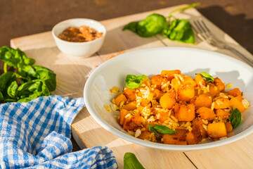 Boiled white rice with fried pumpkin cubes, onion and spices in a round gray plate on a wooden tray. Pumpkin recipes