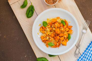 Boiled white rice with fried pumpkin cubes, onion and spices in a round gray plate on a wooden tray. Pumpkin recipes