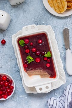 Cold appetizer, tender chicken liver pate with cranberry jelly garnished with cranberries and parsley in a white dish on a light concrete background. Liver recipes.