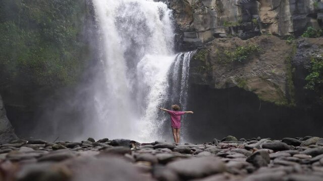 Elegant woman enjoying freshness, tranquility and solitude near a wild streaming waterfall in jungle rocks