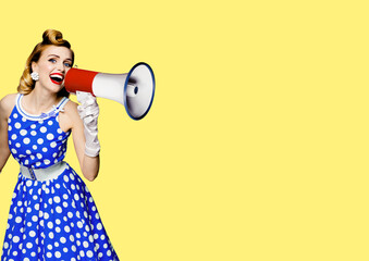 Portrait image of haired woman holding mega phone, shout advertising something. Girl in blue pin up style dress with mega phone loudspeaker. on yellow background. Beauty model in retro fashion concept