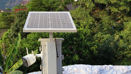 Solar cell panel on top of steel pole. Dusty tiny solar cell panel with CCTV below to run without electricity in the green tree background with copy space. Selective focus; clean energy concept