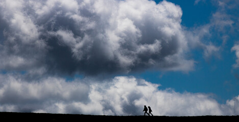 silhouettes de randonneurs au sommet d'une colline devant un ciel bleu nuageux