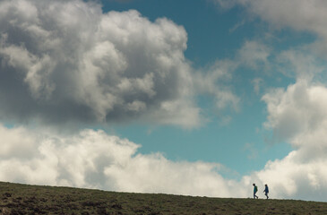 Naklejka na ściany i meble silhouettes de randonneurs au sommet d'une colline devant un ciel bleu nuageux