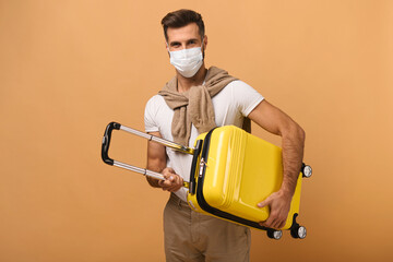 Caucasian man in protective mask holding baggage and looking at the camera while preparing to the traveling isolated on orange background