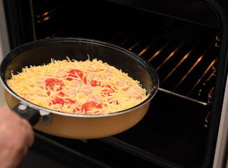 Putting a pan with homemade pizza with sausages, tomatoes and cheese in hot air oven close up with selective focus. Process of cooking pizza, step 10