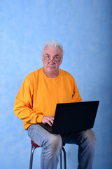 An elderly gray-haired man of retirement age at a laptop on a blue background