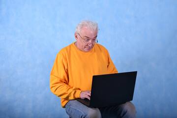 An elderly gray-haired man of retirement age at a laptop on a blue background